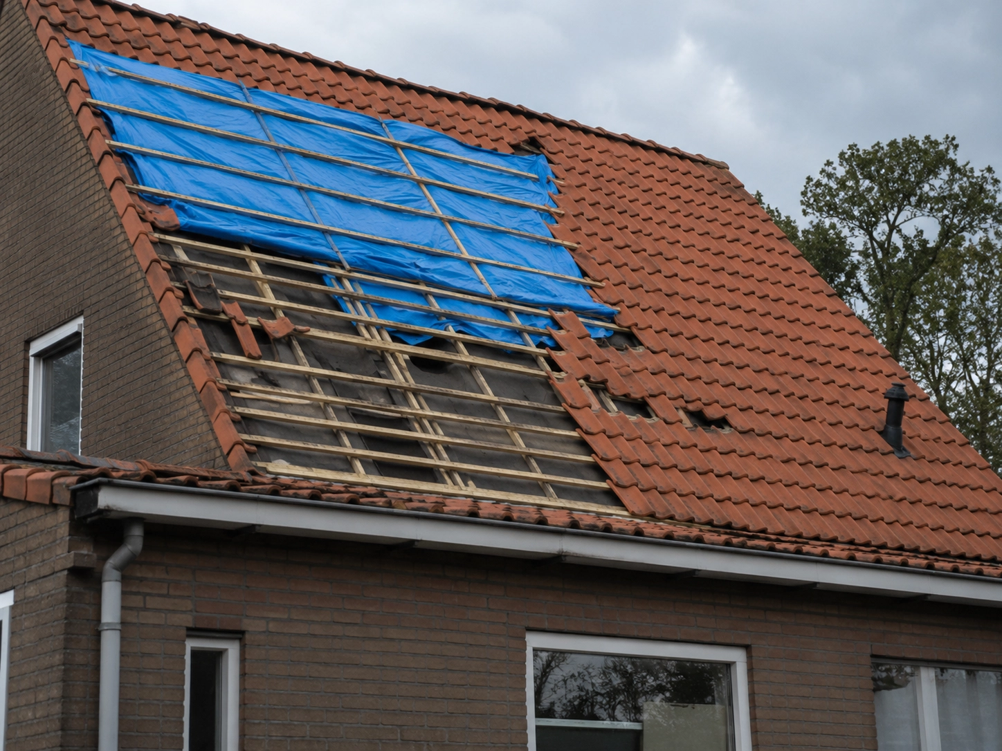 Stormschade aan een pannendak met blauw afdekzeil en ontbrekende pannen